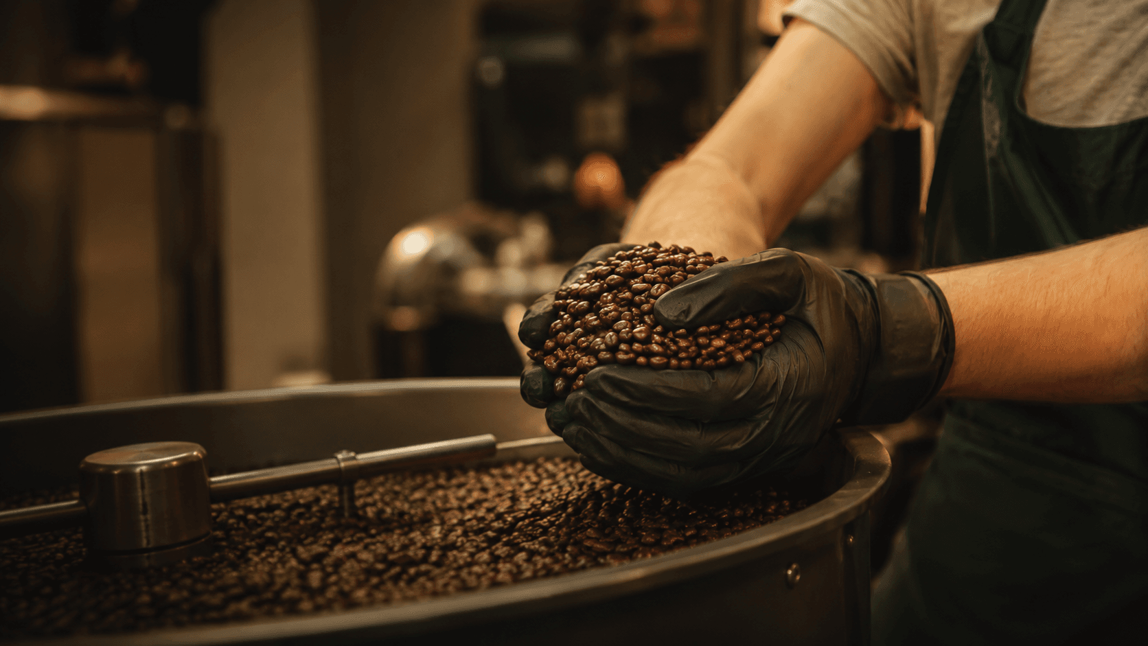 Close-up of a gloved hand cupping fresh-roasted coffee beans over a roaster drum