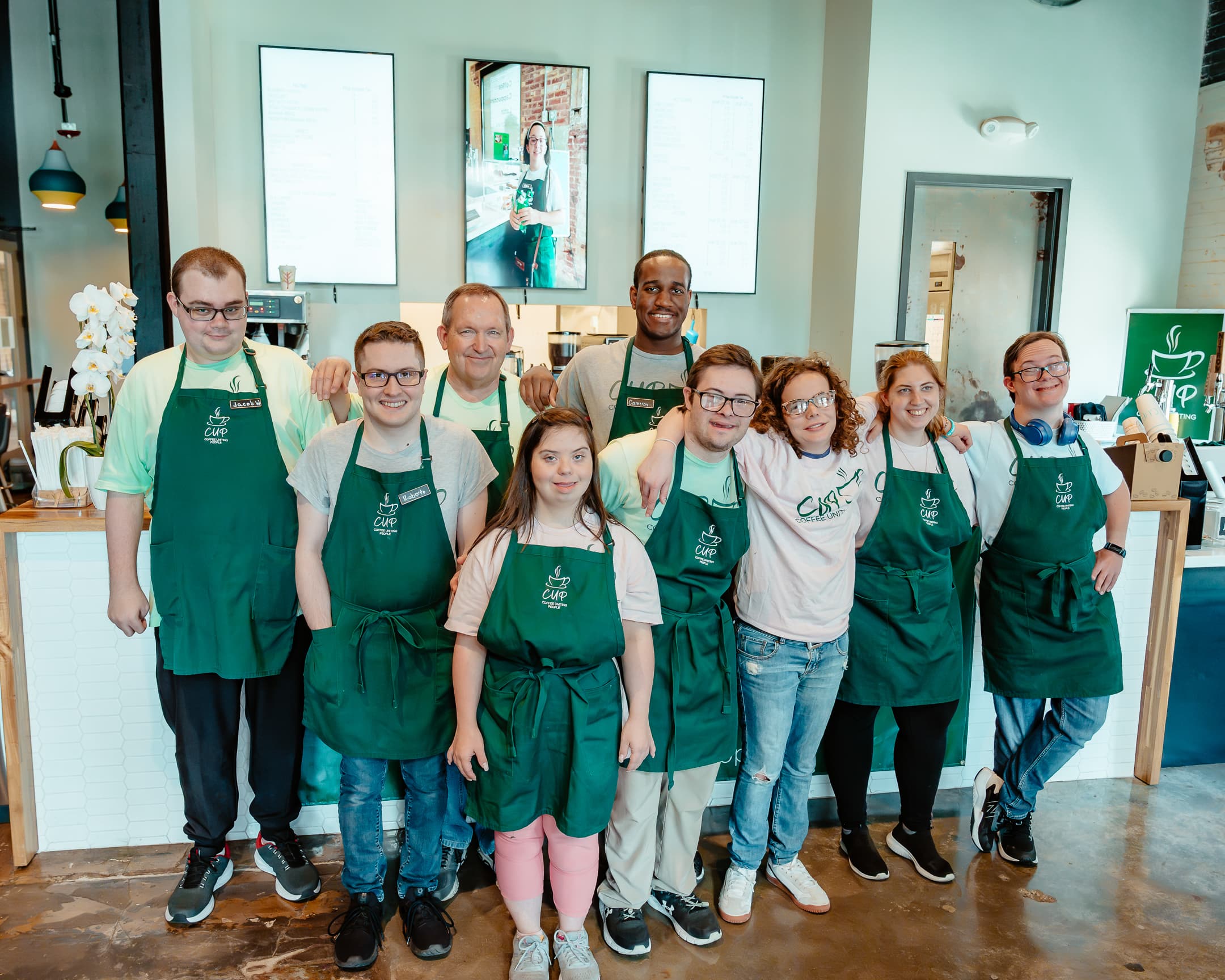 The full Coffee Uniting People team in green aprons gathered at the South Tampa flagship coffee bar