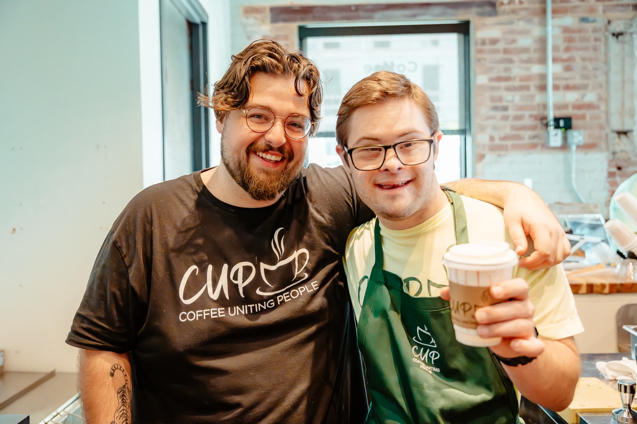 Two CUP team members raising a paper coffee cup in a toast
